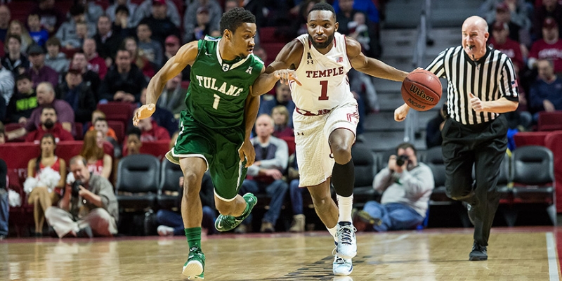 A Temple men s basketball player dribbling a ball as a Tulane player defends.