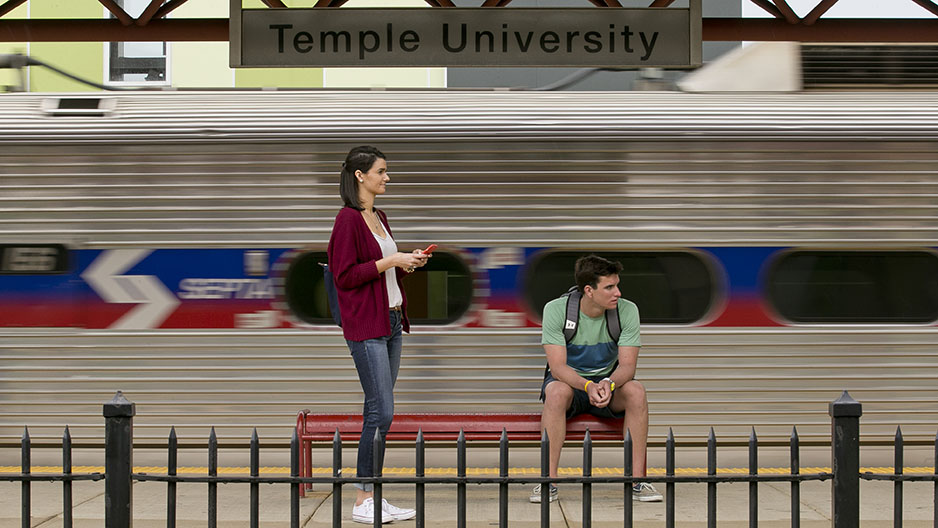 Two students waiting for a train at Temple University s SEPTA Regional Rail Station as a train passes by.