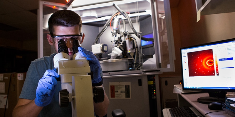 A male researcher looking through a microscope in a lab.