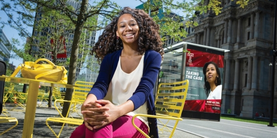 Temple students sits in front of ad that features her.
