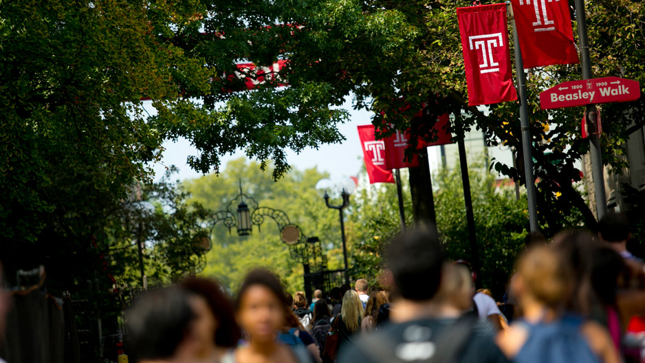 Students walking on campus under Temple T flags.
