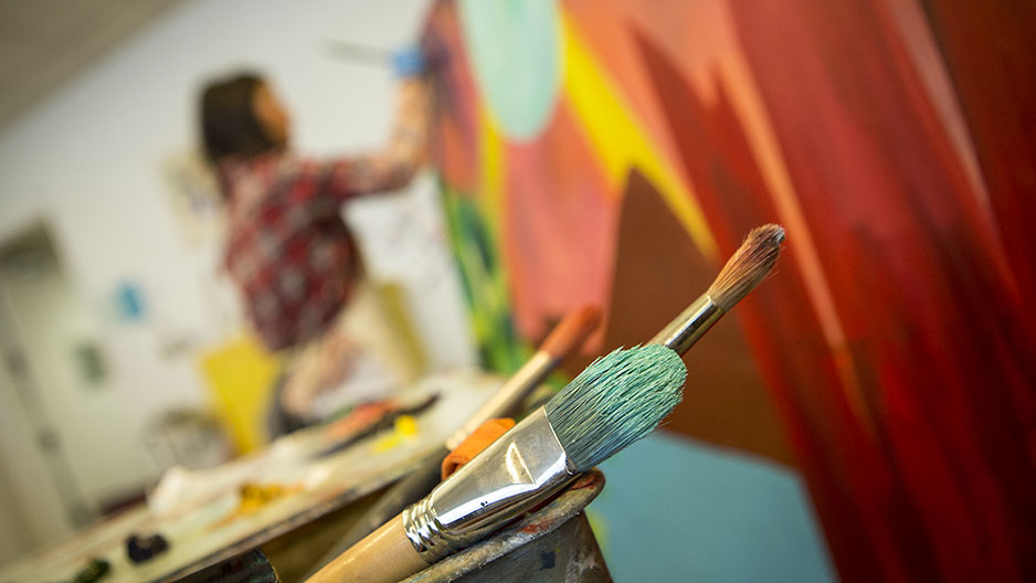 Paintbrushes and a woman painting in the background.