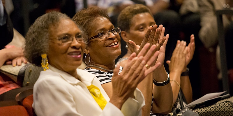 Three women are clapping and smiling.