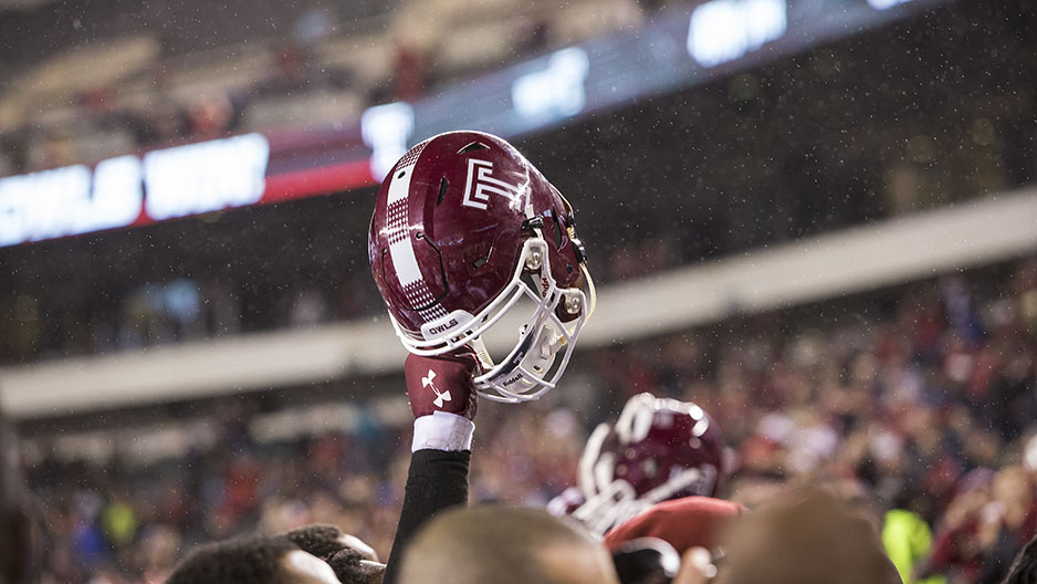 A Temple football helmet held high above a crowd of football players.