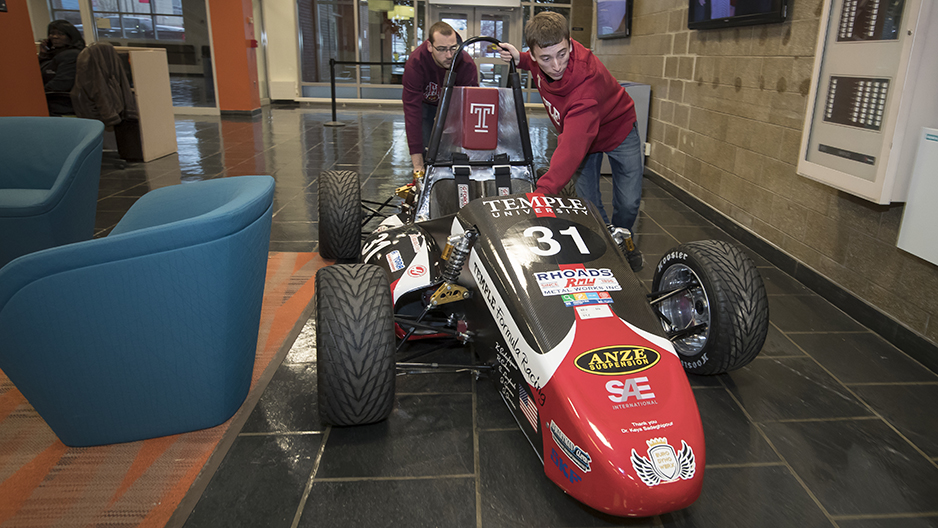 Two students pushing the race car through the engineering building.