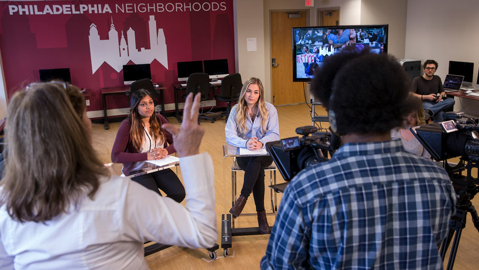 students sitting at an anchor desk and running cameras on a temporary TV set