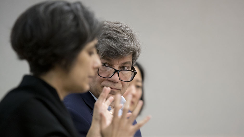 A woman speaking while a man looks at her and listens.