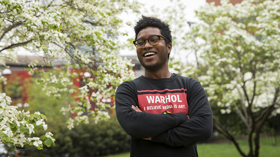 Christopher Persaud standing in front of flowering trees smiling with his arms crossed.