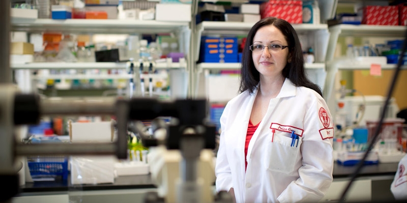 Polina Gross standing at a laboratory bench in a white lab coat.