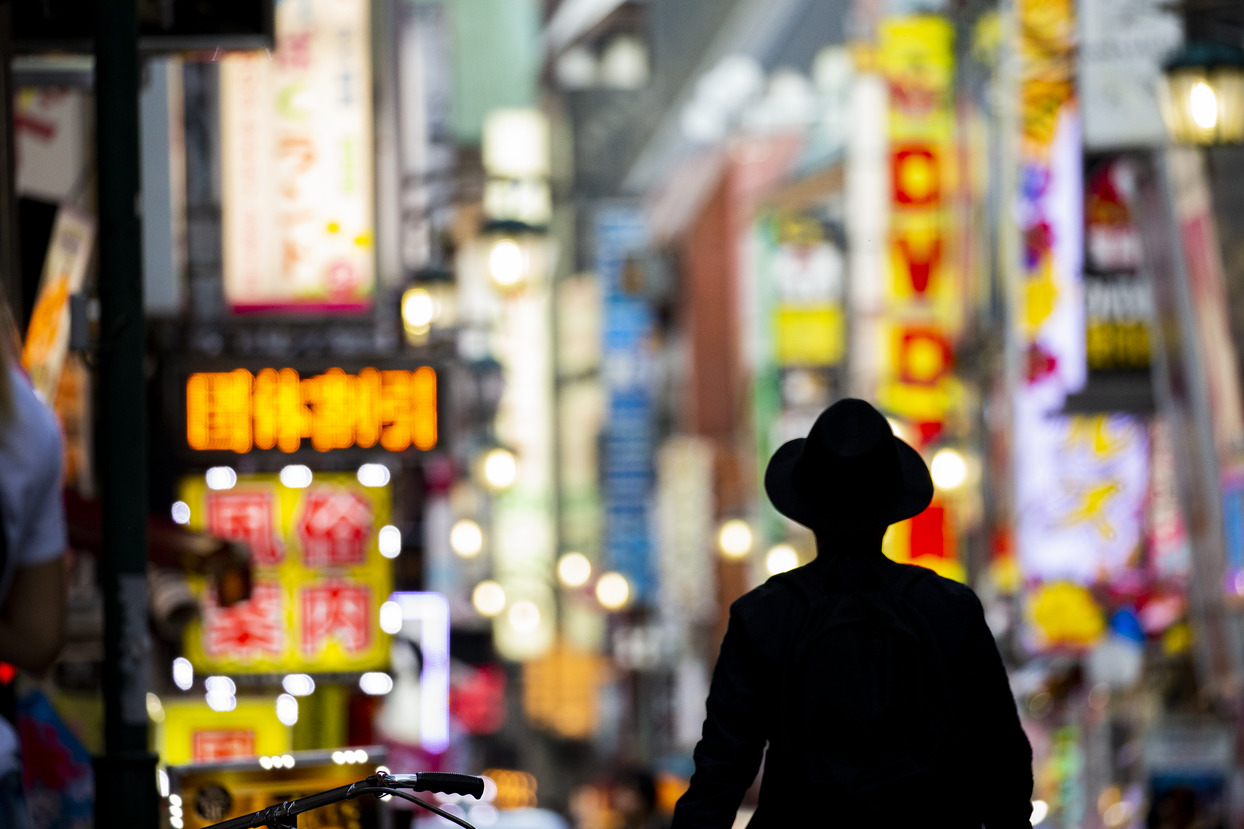 A figure silhouetted against illuminated street signs in Tokyo.