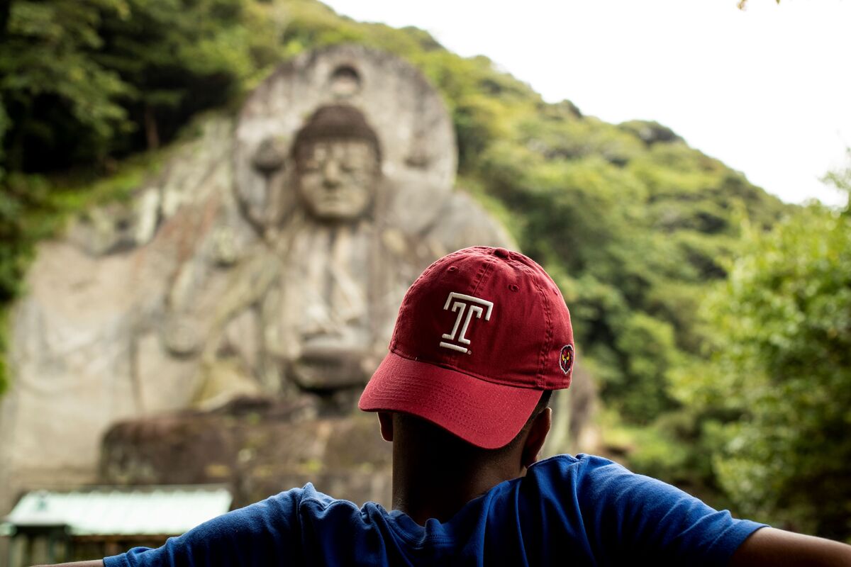 Temple student wearing Temple hat facing Budda statue