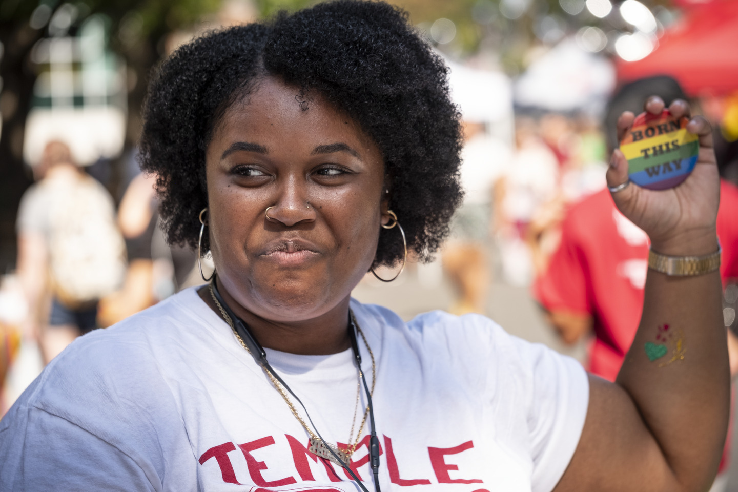A Temple student holding up a rainbow colored pin that says