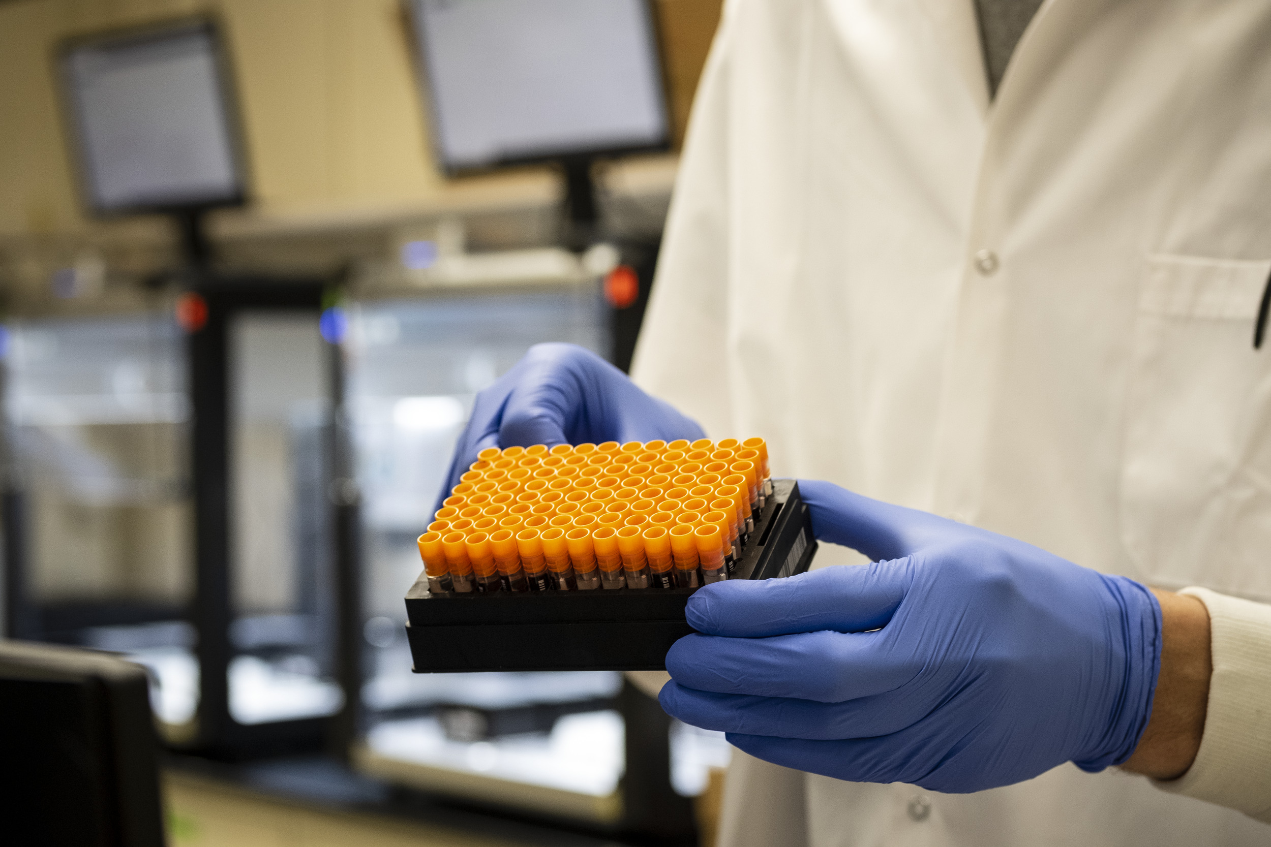 A technician holding a tray of COVID-19 testing sample vials.
