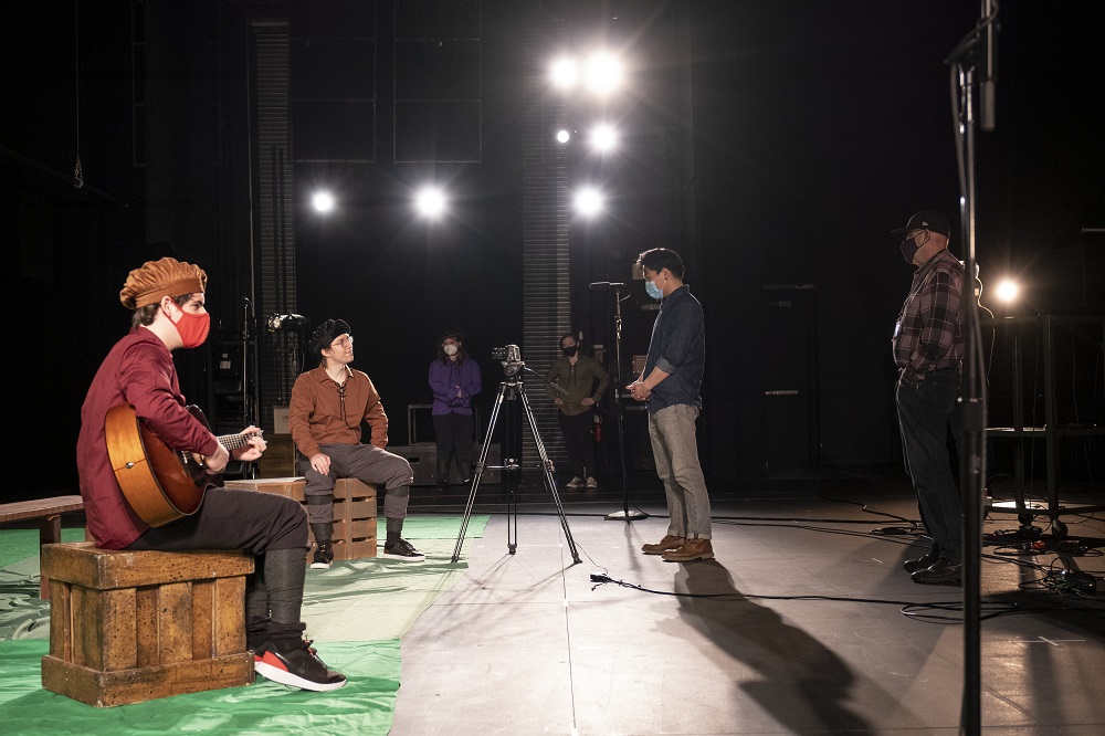 Students and faculty working together to film a theater performance in front of a green screen.