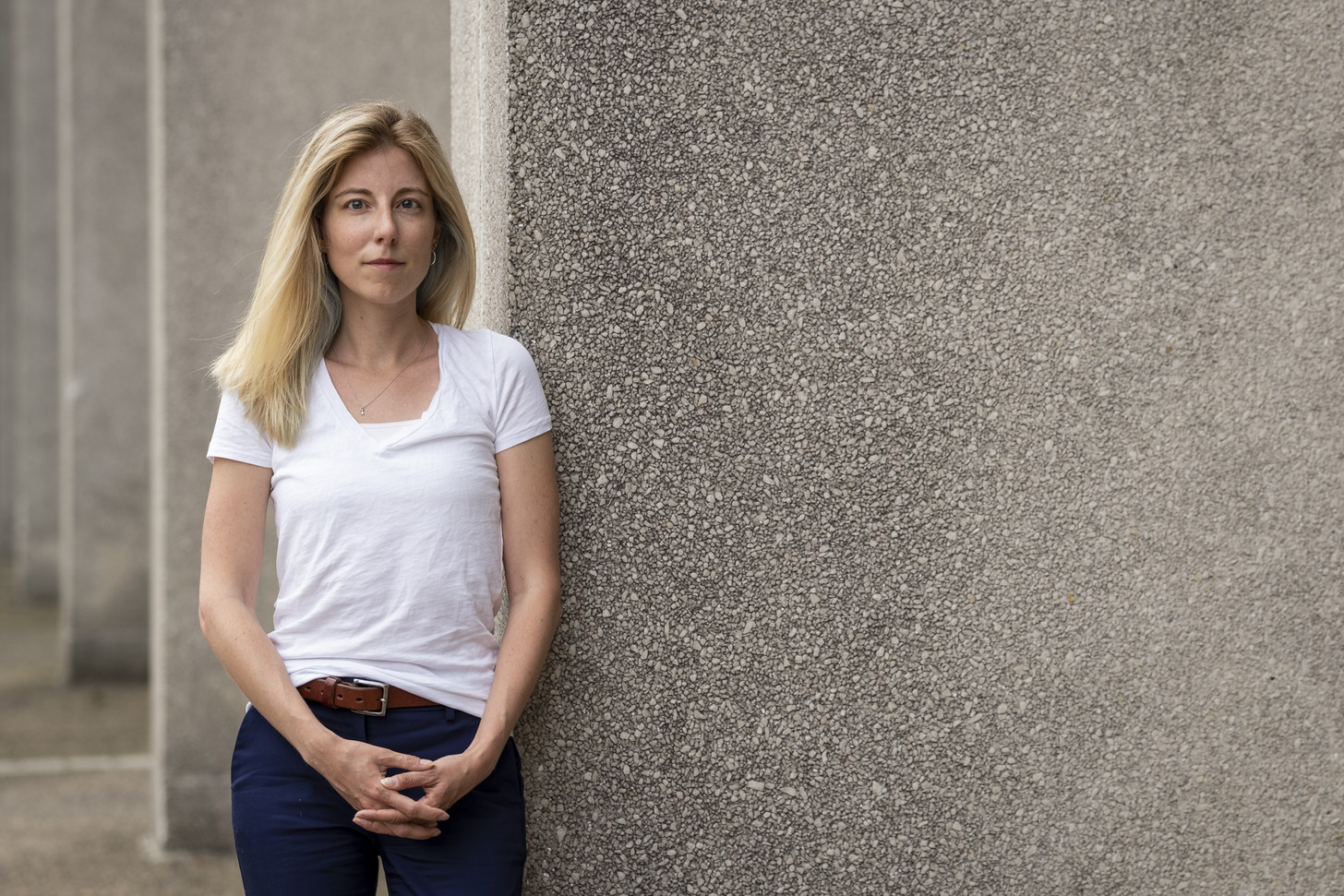 Jennifer Pollitt standing in front of a concrete building, wearing a white t-shirt.