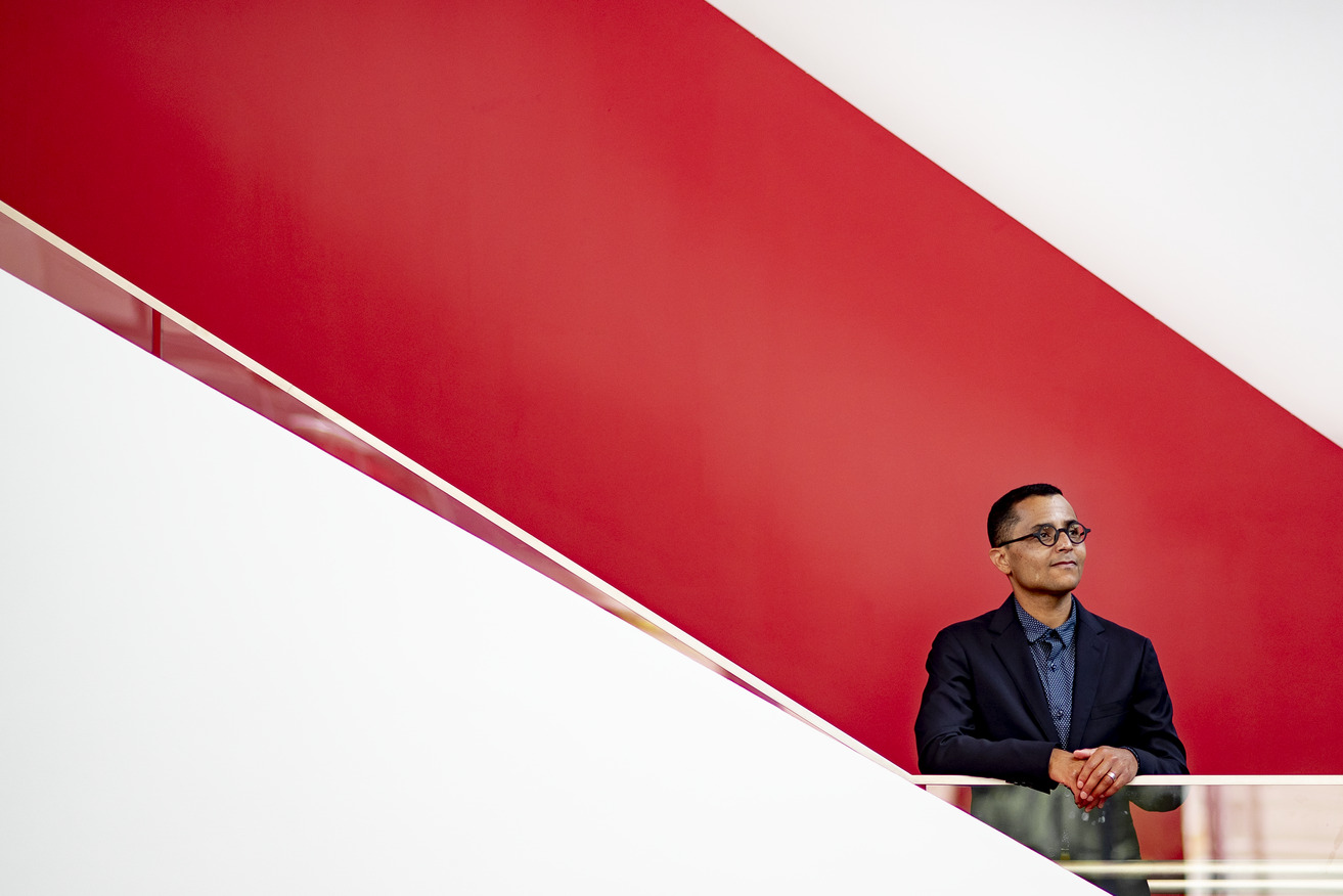 Heath Fogg Davis standing by a staircase with a red background.