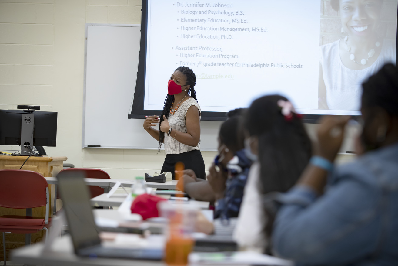A woman in a red face covering standing before an overhead projector screen.