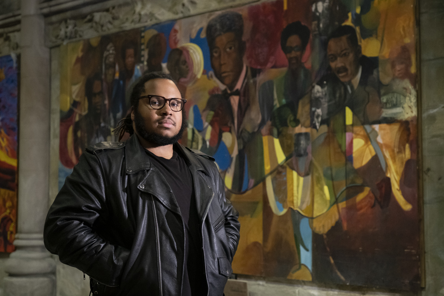 Tyler A. Ray stands in front of one of 14 murals inside the Church of the Advocate.