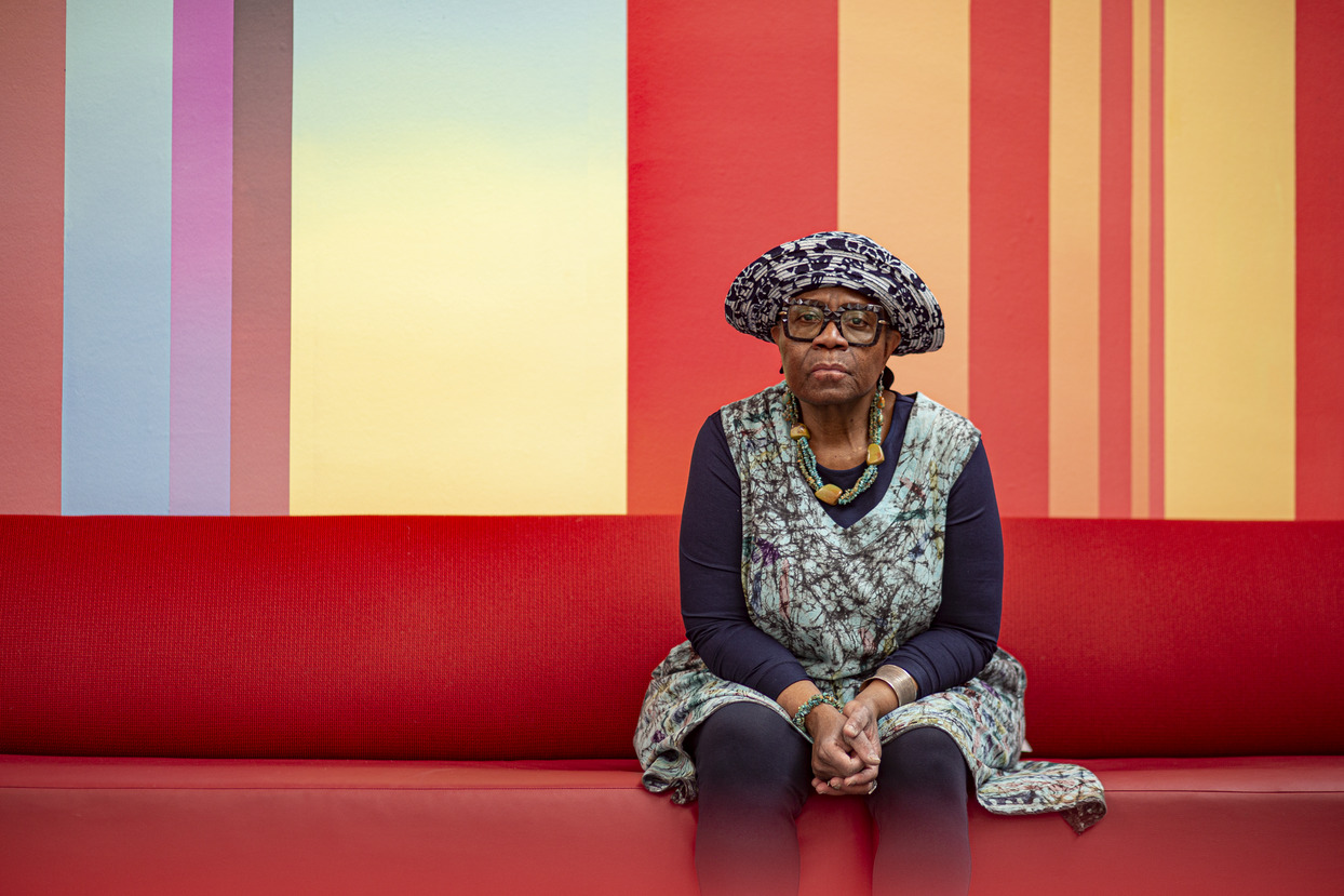 Image of Joyce Joyce on a red couch with a multicolored background.