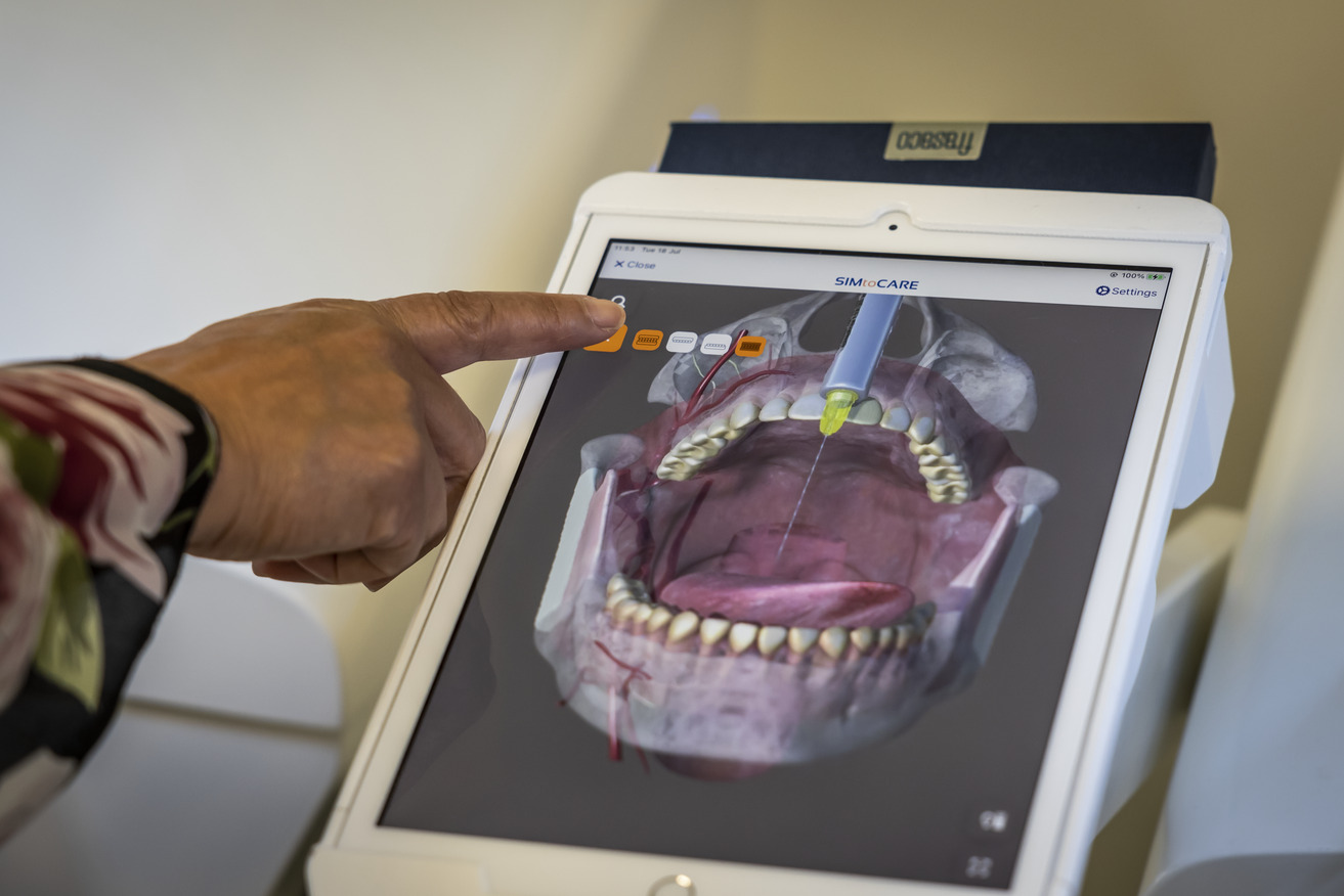 A finger points at a digital model of a mouth on a screen
