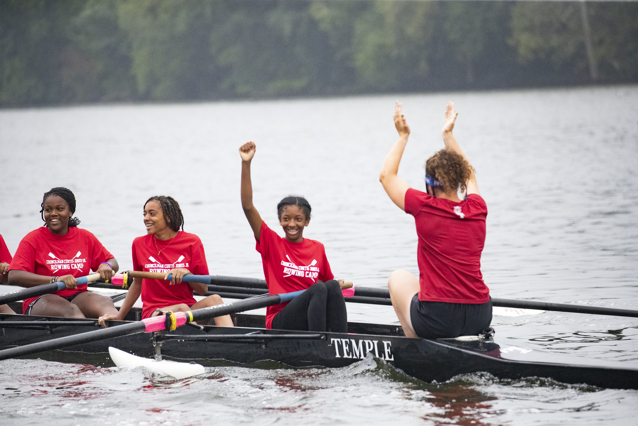 Image of children with smiles wearing red t-shirts, rowing a boat.