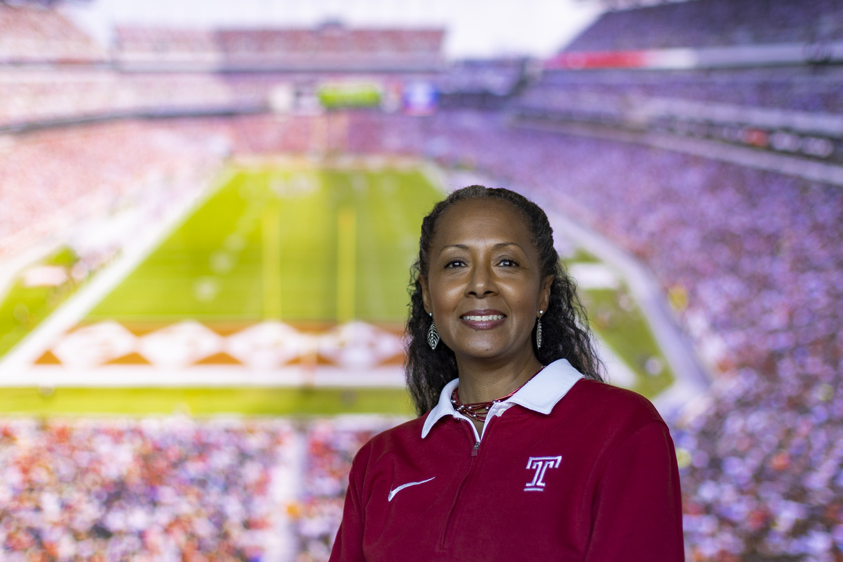 A woman wearing a cherry and white Temple shirt pictured with the background of Lincoln Financial Field.