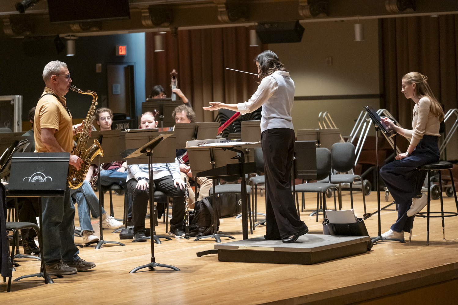 Image of Matthew Levy soloing with the wind symphony. Patricia Cornett conducts while Emma O'Halloran observes.