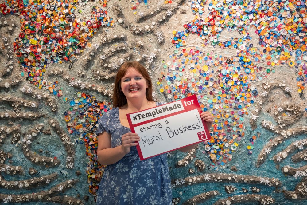 Abigail McNavage holding a #TempleMade sign in front of her painting