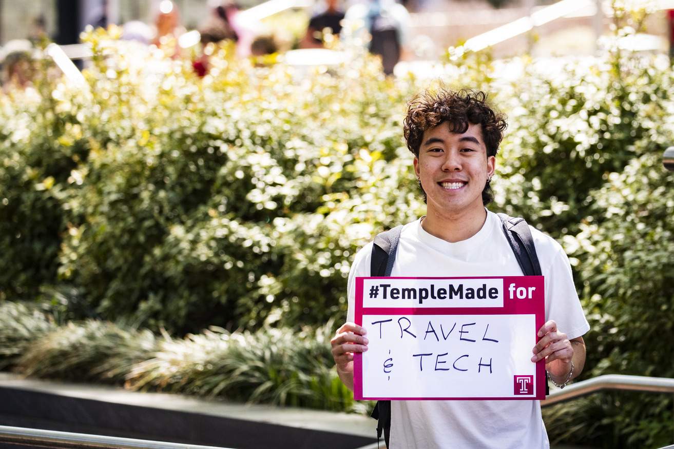Image of Tran holding a sign that says #TempleMade for travel and tech