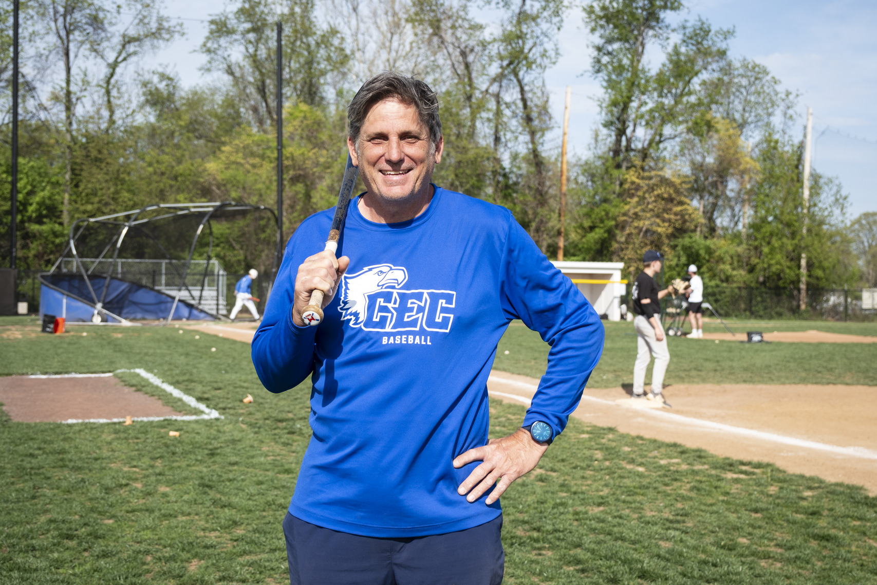 Image of a person wearing a blue shirt and holding up baseball bat on a field.