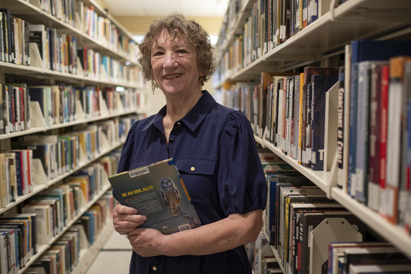 Sandi Thompson standing in the book stacks with a book in her hands at Ambler Campus Library