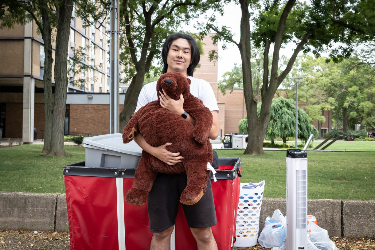 A student stands in front of J&H hugging a large stuffed bear.