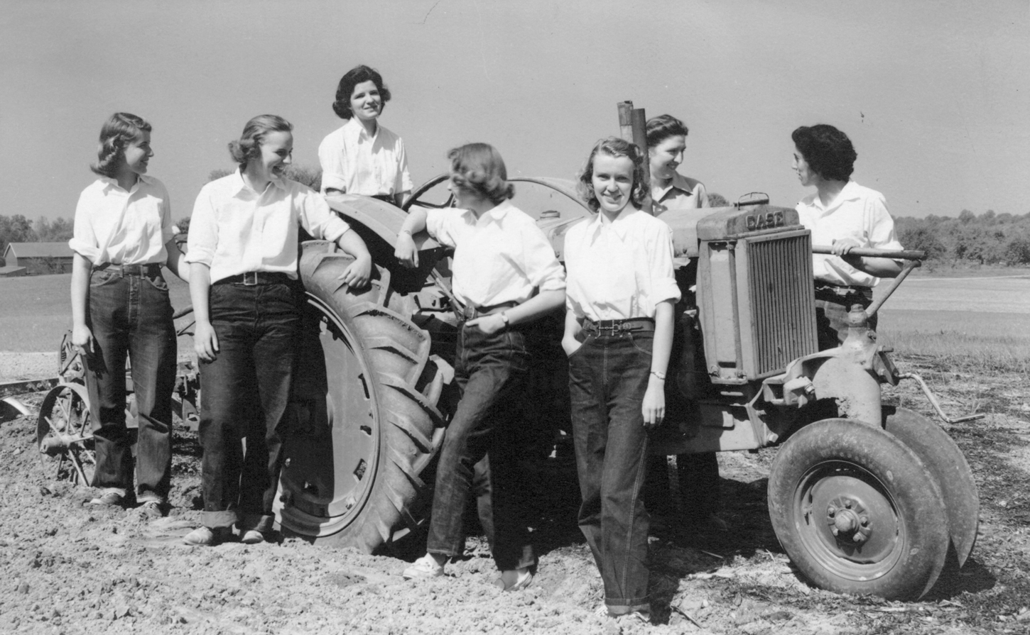 A black and white photograph of women in horticulture standing around a tractor in the field.
