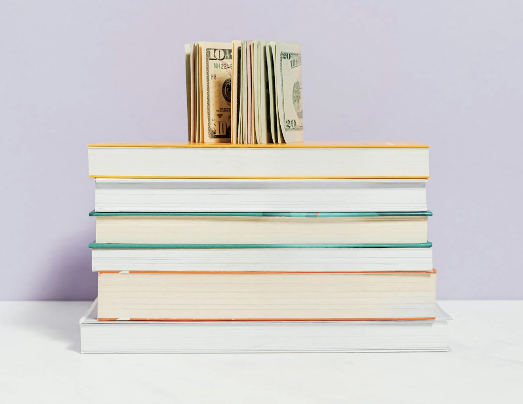 A stack of books with a group of paper currency propped up on top