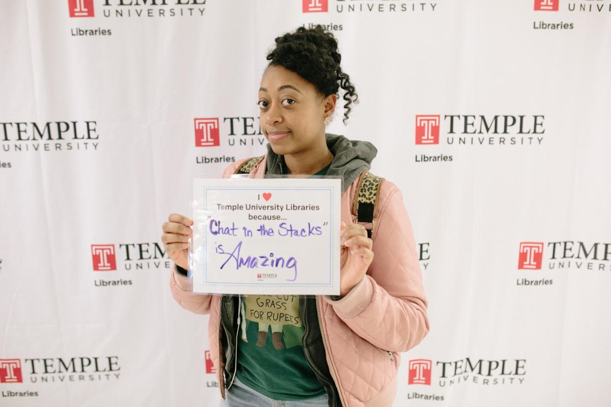 photo of Temple student with sign that reads: I love the Libraries because Chat in the Stacks is amazing.