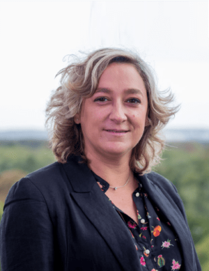 image of Florence wearing a floral blouse and black blazer standing outside smiling at the camera