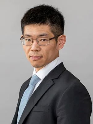 image of Ohyun wearing a blue suit and tie and glasses looking at the camera
