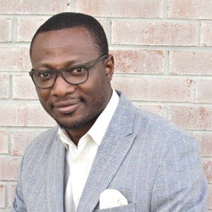 image of Oluwayomi wearing glasses, a grey suit, short cut hair looking at the camera
