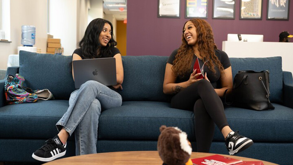 Two Temple students sitting on a couch laughing.