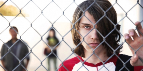 A male teen from the documentary The Bad Kids holding a chain link fence.