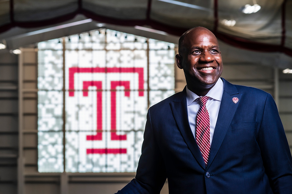 Arthur Johnson, in suit, smiling in front of Temple logo