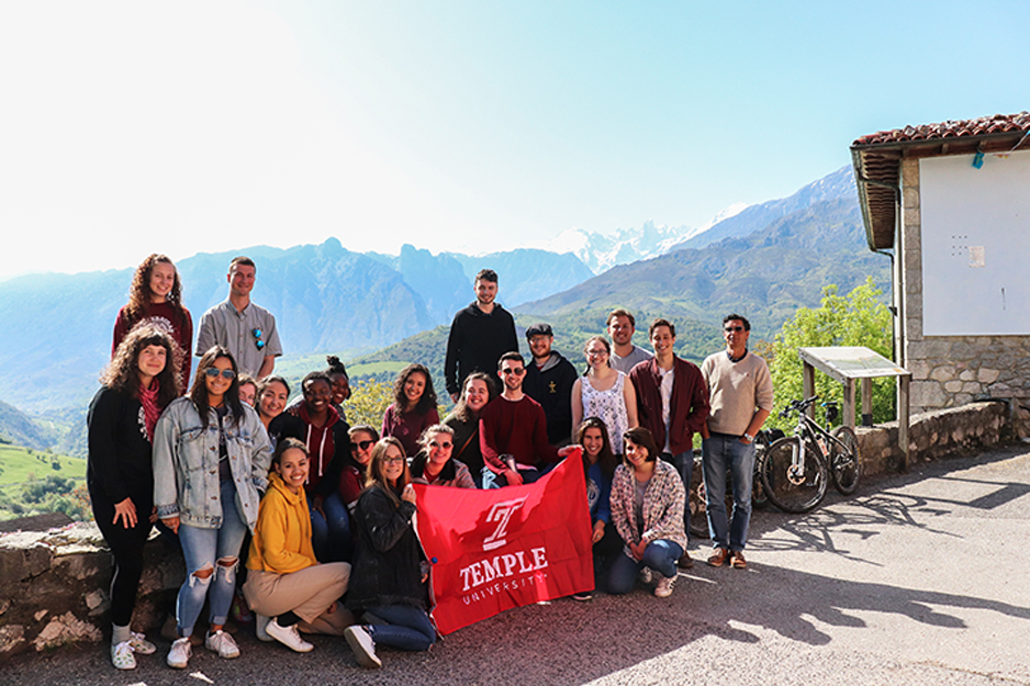 Mountains in the background, a group of Temple students holding a Temple cherry flag.