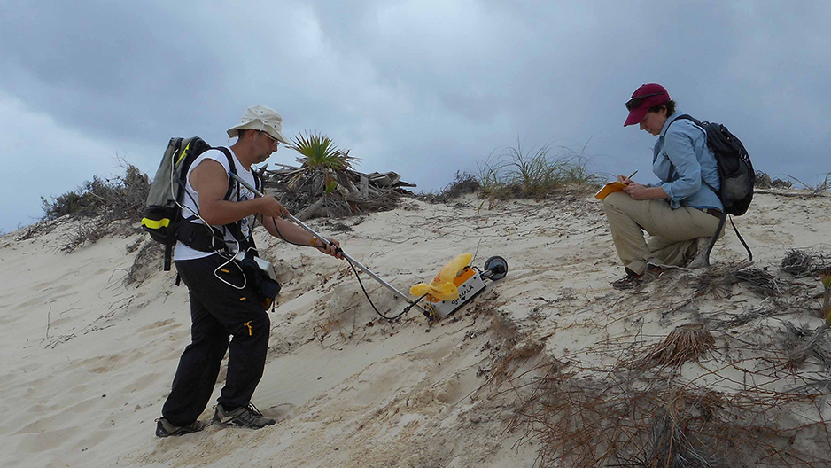 A man using a yellow georadar machine on a beach.