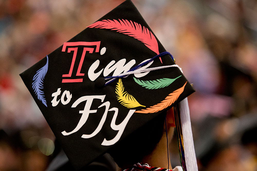 A Temple graduate triumphantly raising his cap at commencement.