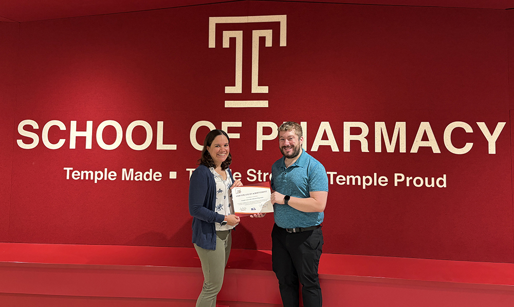 Faculty co-advisors in front of a red wall with the Temple T and the award