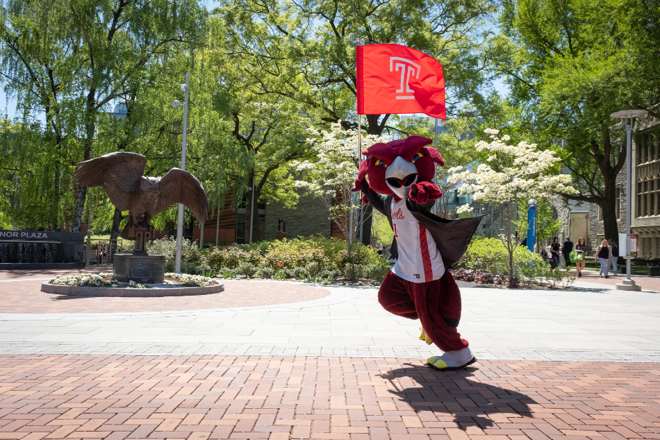 Hooter carries the Temple flag as he runs past the owl statue and points at the camera