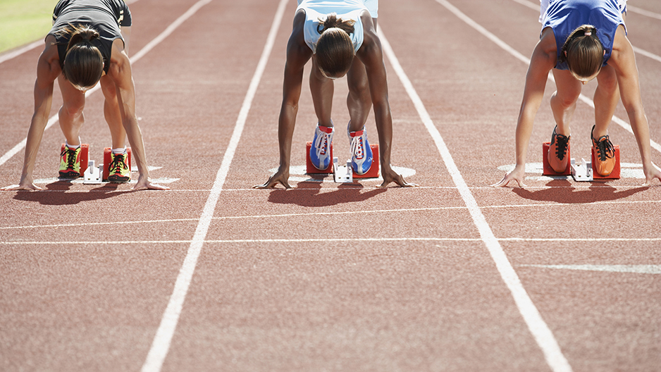 Women runners kneeling on the track before a race starts.