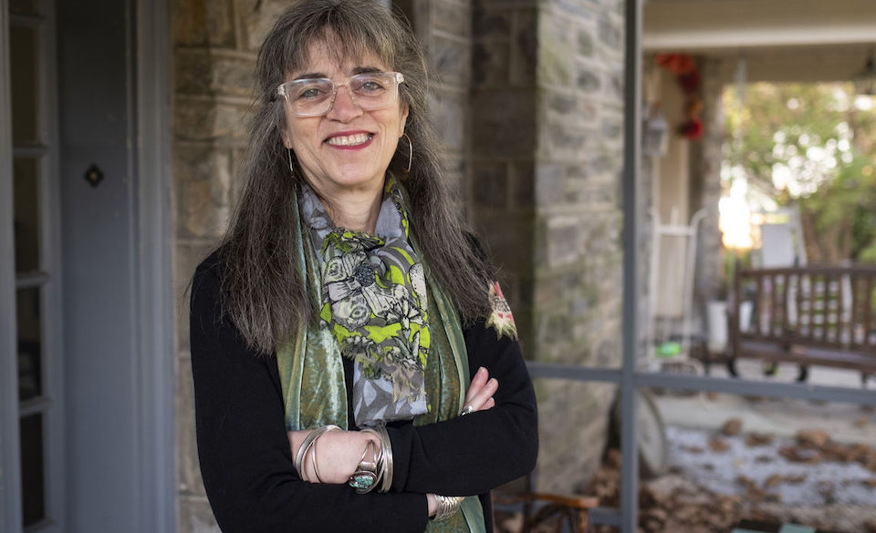 image pf Laura standing outside wearing a black top, green blouse and glasses with her arms crossed smiling at the camera