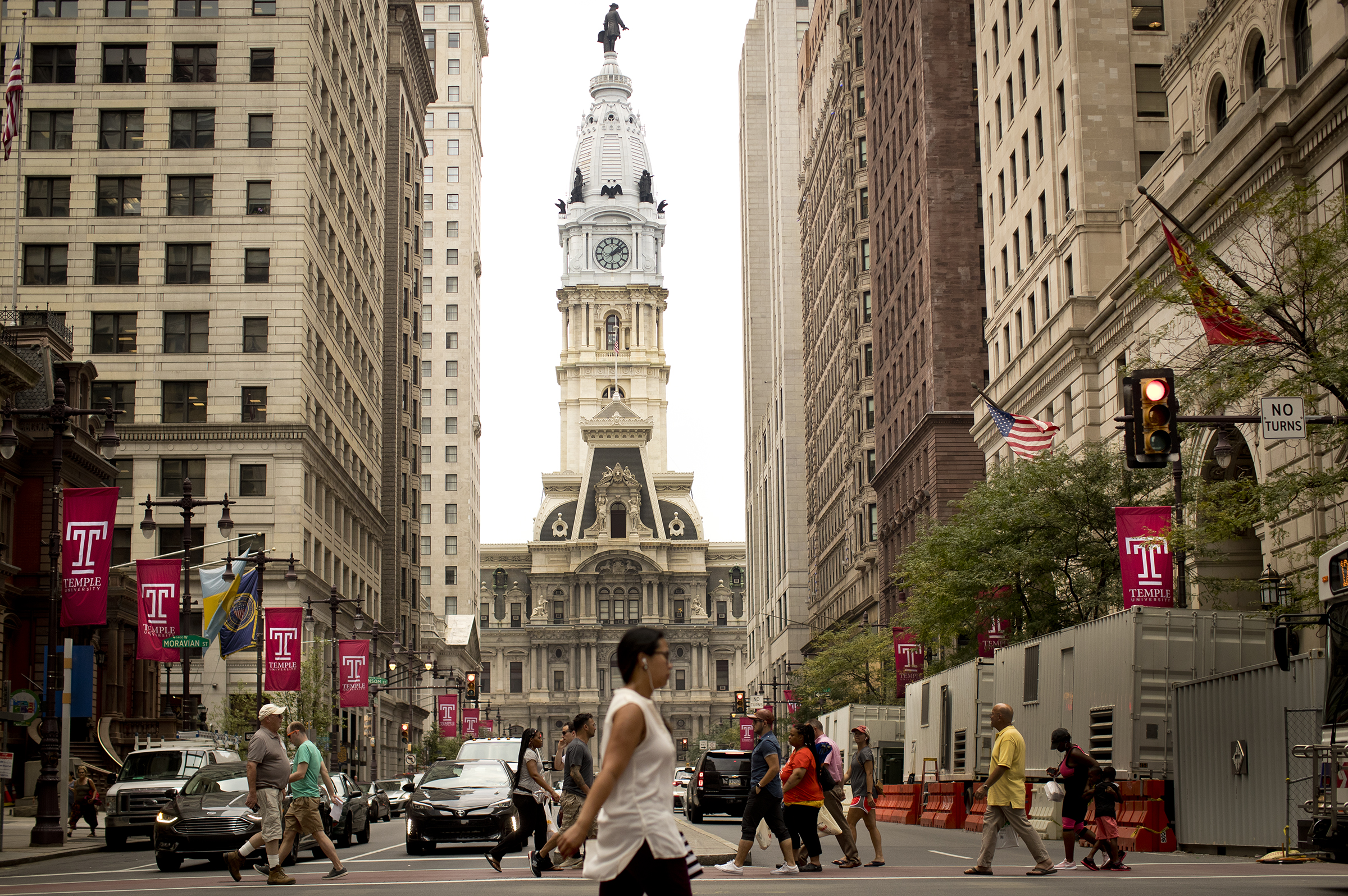 Looking down Broad Street with City Hall flanked by buildings on either side with Temple lamppost flags along the street and pedestrians crossing