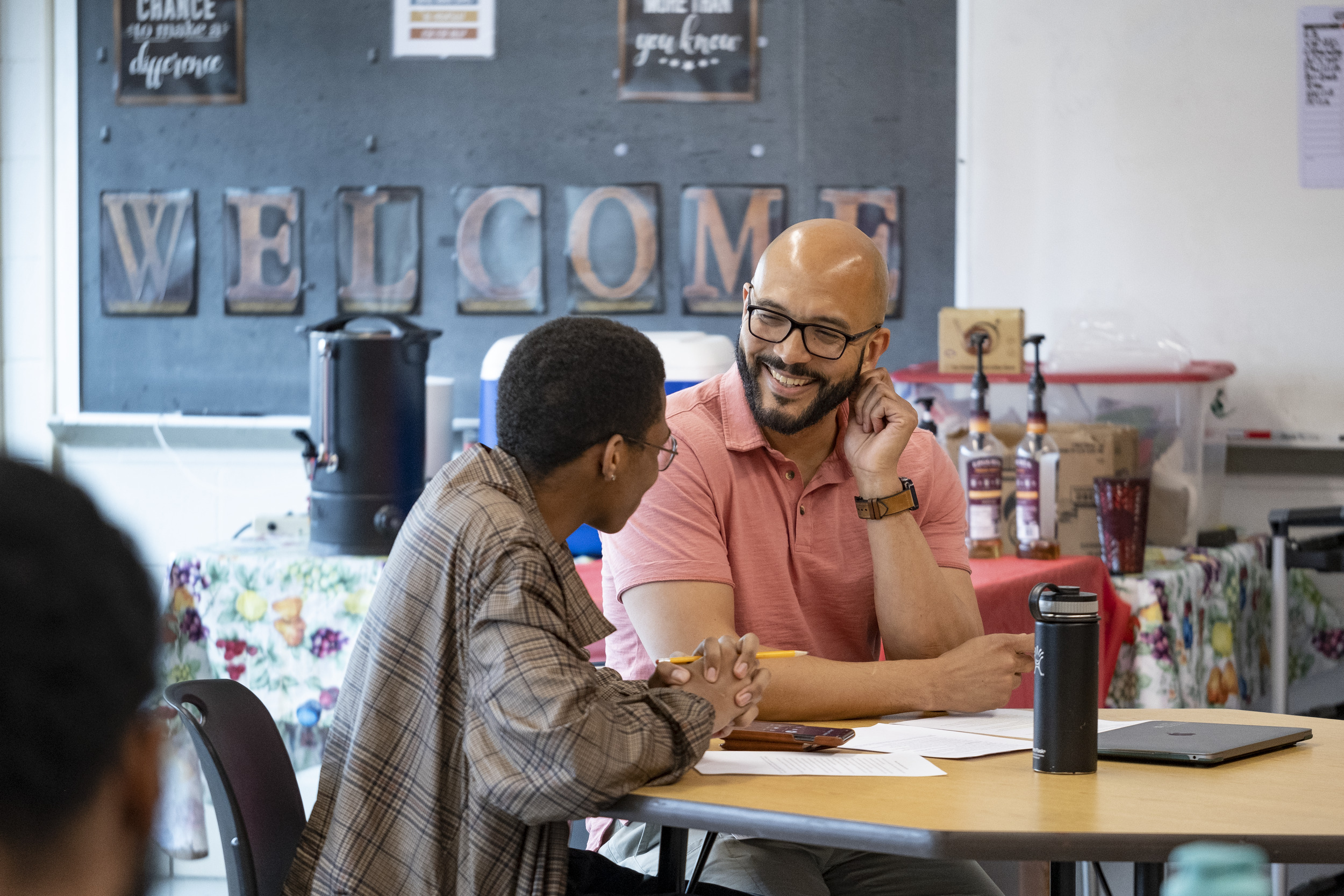 A teacher sits at a table with a student in a classroom